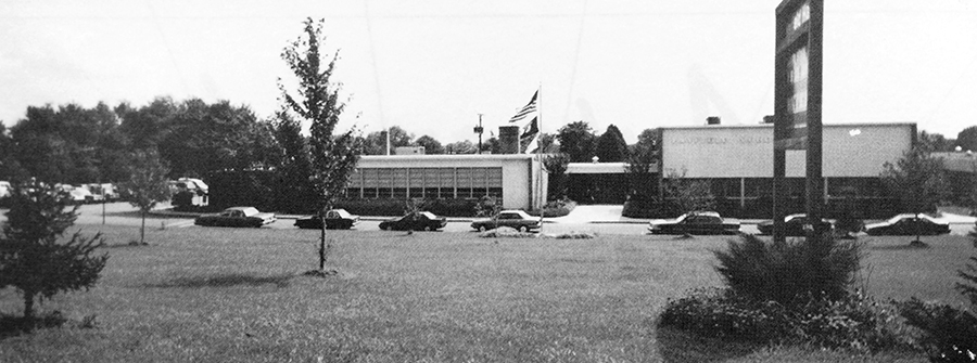 Black and white photograph of the front of Hayfield Elementary School from our 1993 to 1994 yearbook. The building was photographed from the sidewalk along Telegraph Road. A row of cars is parked in the bus loop in front of the school.  